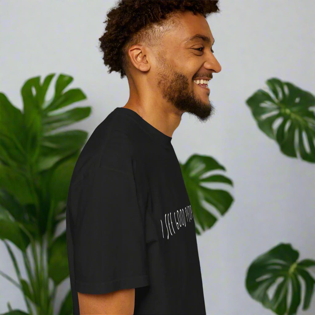 Side profile of a smiling man wearing a black 'I See Good People' unisex t-shirt. The minimalist white text design on the garment-dyed fabric highlights the t-shirt's relaxed fit and casual style, perfect for spreading positivity.