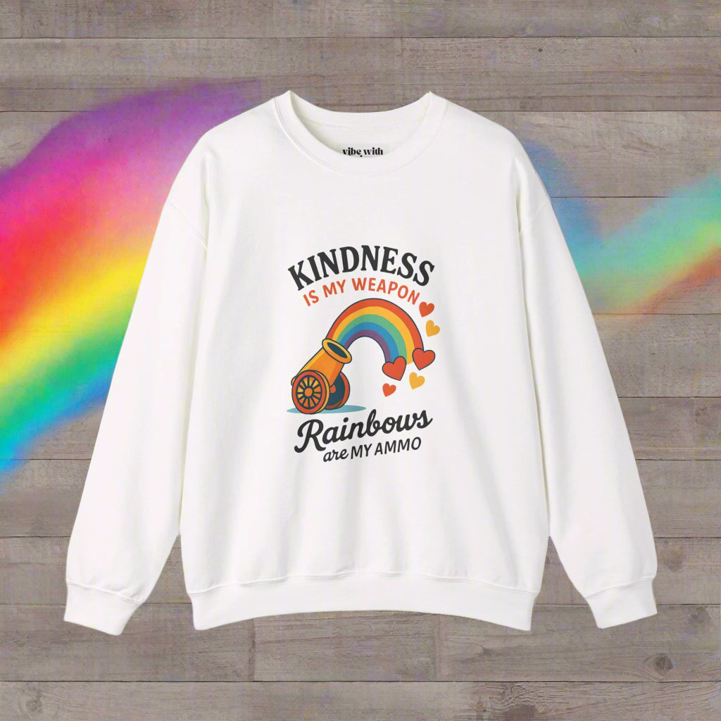A white crewneck sweatshirt featuring the colorful design 'Kindness is My Weapon, Rainbows are My Ammo,' with a cannon shooting a vibrant rainbow and hearts. This bold and uplifting design celebrates positivity, unity, and LGBTQ+ pride, perfect for spreading good vibes.
