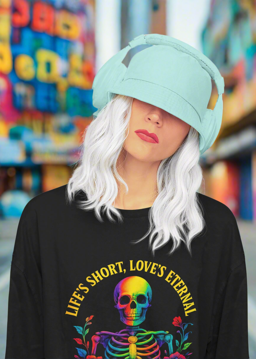 Model wearing the 'Life's Short, Love's Eternal' rainbow skeleton shirt from the ONE collection by Vibe with Kindness. Styled with aqua bucket hat headphones and white hair, the look radiates boldness and individuality, celebrating unity, love, and positivity.