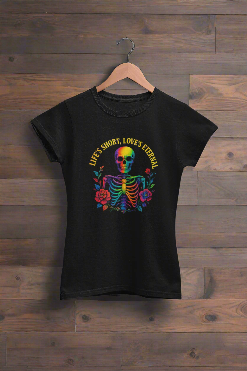 Black t-shirt featuring the 'Life's Short, Love's Eternal' rainbow skeleton design from the ONE collection by Vibe with Kindness. The bold design includes a colorful skeleton surrounded by roses, symbolizing love, unity, and LGBTQ+ pride, displayed on a wooden hanger.